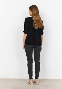 Musta, pitkähihainen paita, jossa käännetyt hihat, yhdistetty mustiin skinny-farkkuihin. Mallilla on päällä hopeiset sandaalit, nähtynä takaa.