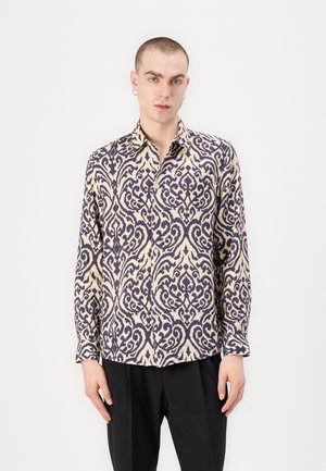 Long-sleeve shirt with a cream and navy pattern, featuring a collared neckline and button front. Fabric has a smooth texture.
