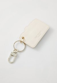 Cream leather keychain with a textured edge, featuring a gold metal ring and clasp, embossed brand logo on the surface.