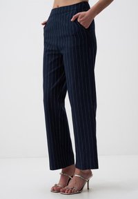 Marineblauwe pinstripe broek met een getailleerde pasvorm, voorzien van zijzakken en een rechte pijp, gemaakt van een gladde stof.