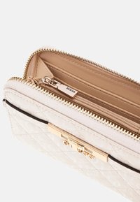 Portafoglio crema trapuntato con dettagli in oro, dotato di chiusura con zip e interno in pelle. Include una tasca interna con zip e slot per carte.