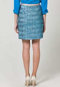 Blå paljettmini kjol med en figursydd design och texturerad yta, parat med vita högklackade skor. Synlig bakvy och nederkant ovanför mitten av låret.