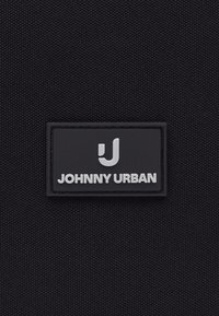 Tessuto nero intrecciato con una toppa rettangolare nera con il logo stilizzato bianco "J" e il testo "JOHNNY URBAN".