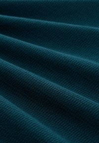 Teal textiel met een wafelpatroon, met rimpels en plooien, die een zachte maar gestructureerde uitstraling van het materiaal laat zien.