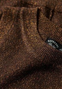 Maglione marrone lavorato a maglia con una finitura a trama e fili metallici dorati. Presenta un colletto a costine e un'etichetta del brand ben visibile.