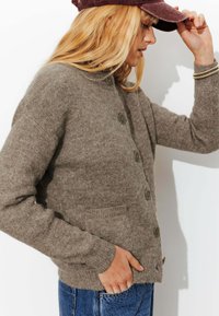 Cardigan en laine marron avec un col rond, fermeture à boutons et deux poches avant. Tissu texturé et chaud avec poignets et ourlet côtelés.