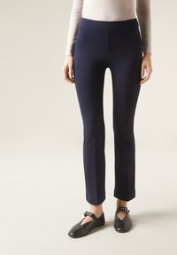 Marinblå tights med en figurnära design och en slät textur, med ett brett midjeband och raka ben, parat med svarta ballerinaskor.