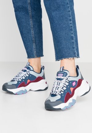 Person wearing colorful chunky sneakers with navy, gray, pink, and white panels, paired with cuffed blue jeans.