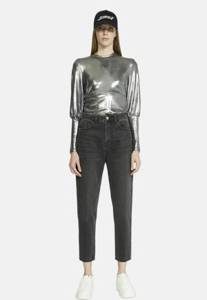 Top in argento metallizzato a maniche lunghe con spalle arricciate, abbinato a jeans neri a vita alta e sneakers bianche. Un cappello scuro completa il look.