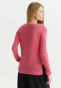 Różowy sweter z długim rękawem o okrągłym dekolcie, z teksturowanej tkaniny, lekko luźny krój oraz z rozporkiem z tyłu.