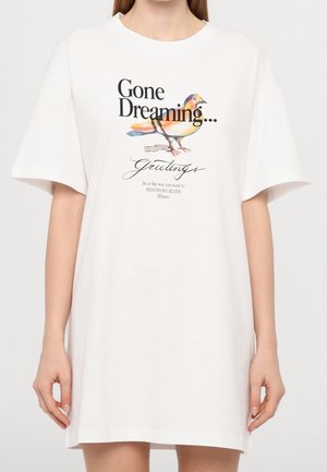 Witte oversized T-shirtjurk met een kleurrijke vogelillustratie en de tekst "Gone Dreaming… Greetings" aan de voorkant.
