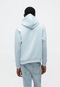 Lys blå hettegenser med snøring i hetten, ribbede mansjetter og kant, myk tekstur, brukt sammen med lyseblå denimjeans.