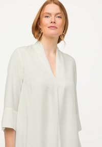Weiße, leichte Bluse mit tiefem V-Ausschnitt und Ärmeln bis zum Ellenbogen, die eine glatte Textur und ein minimalistisches Design aufweist.