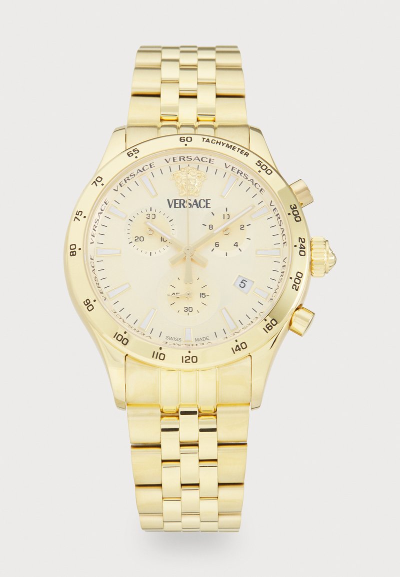 Reloj cronógrafo dorado con una correa de metal texturizada, un dial crema y acentos en tono plateado; presenta una escala taquimétrica y una ventana de fecha.