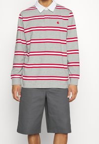 Langärmliges graues Polohemd mit roten und weißen Streifen, ausgestattet mit einem weißen Kragen und einem kleinen Logo auf der Brust, kombiniert mit grauen Shorts.