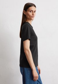 Zwarte T-shirt met korte mouwen en een ronde hals, gemaakt van zachte stof, gecombineerd met blauwe denim jeans, zijaanzicht weergegeven.