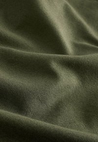 Tissu texturé en vert olive, présentant une surface tissée ; les plis et les rides créent de la profondeur et une variation dans la réflexion de la lumière.