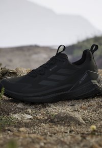 Scarpa da trail running Adidas Terrex nera con tomaia Gore-Tex, suola robusta e linguette per la trazione, posizionata su terreno roccioso all'aperto.