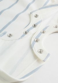 Belo in svetlo modro tkanino z navpičnimi črtami in pritiskači. Mehka tekstura, ukrivljen izrez in vidni detajli roba.