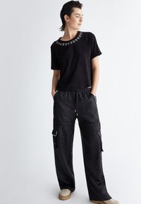 T-shirt nera in cotone con scollo decorato abbinata a pantaloni cargo neri con motivo, dotati di tasche e vita con coulisse. Calzature color crema.