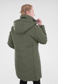 Manteau matelassé vert olive avec capuche, présentant un quilting en chevrons au dos et une texture lisse. Cordon de serrage visible au niveau du cou.