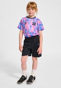 Kortärmad tröja i lila och rosa mönster med svarta accenter, nummer 12, i kombination med svarta shorts och svarta sneakers, vita ankelsockor.