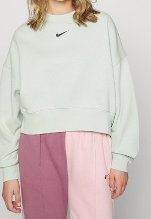 Osoba w jasnozielonym krótkim swetrze Nike i dwukolorowych spodniach dresowych w kolorze mauve i jasnoróżowym z logo Nike.