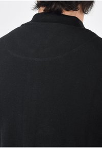 Schwarzer Pullover mit strukturiertem Muster und Rippendesign, ausgestattet mit einem runden Kragen und feinen Steppnähten im Nacken- und Schulterbereich.