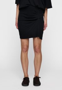 Falda de algodón negra con detalles fruncidos en un lado, hasta la rodilla, combinada con zapatos oscuros de cordones. Diseño sencillo, look casual.