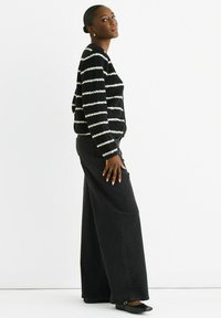 Black and white striped cardigan in textured knit, buttoned at the front. Paired with wide-leg black jeans and flat black shoes.