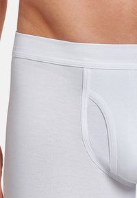 Boxer brief bianchi in cotone con una texture liscia, vita piatta e design della tasca sagomata, parzialmente visibili sulla pelle.