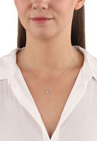 Silverfärgad stjärnhalsband på en delikat kedja, med två små stjärncharms, bärs över en vit kragskjorta. Enkelt och elegant design.