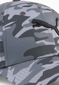 Casquette camouflage grise en tissu texturé, avec une visière courbée et un logo noir brodé à l'avant. Présente une couture sur la visière.