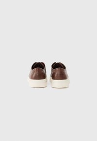Baskets en cuir marron avec une texture lisse, bout arrondi et semelles en caoutchouc blanc contrastant. Design minimaliste, sans logos visibles.