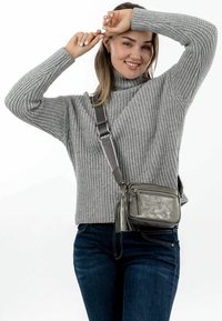 Kompaktní šedá kožená crossbody taška s texturovaným povrchem, zipovým uzávěrem a bočními třásněmi, nošená přes šedý svetr a džíny.