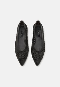 Ballerines noires avec un dessus tressé, un bout pointu et un accent en cuir lisse au niveau des orteils. Intérieur doublé avec une étiquette discrète à l'intérieur.