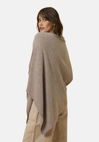 Poncho marrone chiaro realizzato in materiale morbido e texturizzato. Presenta un design sciolto e drappeggiato con una forma triangolare e bordi affusolati.