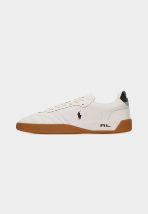 Balta zema profila čības ar brūnu gumijas zoli, melnu Polo Ralph Lauren logotipu sānos un "RL" tekstu papēža daļā.