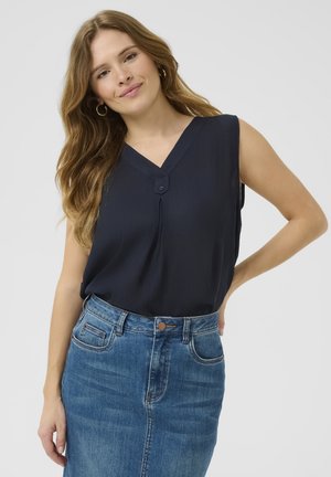 Top sans manches bleu marine avec un décolleté en V, présentant un détail de bouton à l'avant. Porté avec une jupe crayon en denim bleu. Texture lisse, design décontracté.