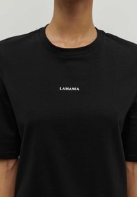 Černé bavlněné tričko s kulatým výstřihem a krátkými rukávy, na hrudi s bílým potiskem "LAMANIA". Hladká textura.