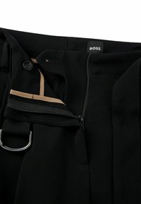 Svarta byxor med dragkedja, knappstängning, beige foder och en silver D-ring detalj på midjan.