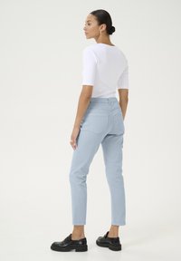 Pantalons ajustés bleu clair en tissu mélangé coton, agrémentés de poches et d'une silhouette slim, associés à un haut blanc ajusté et des chaussures noires.
