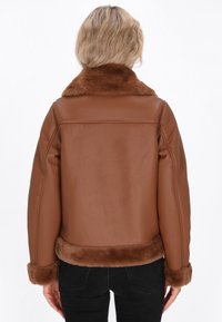 Giacca in finta pelle marrone con collo e polsini in pelliccia, caratterizzata da un design pulito nella parte posteriore e una texture morbida. Vestibilità aderente con una silhouette semplice.