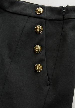 Zwarte rok met een gladde textuur, voorzien van vier decoratieve gouden knopen met gedetailleerde ontwerpen en een ritssluiting aan de zijkant.