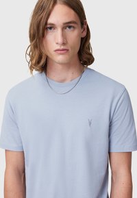 Light blue cotton t-shirt featuring a crew neckline, short sleeves, and a small embroidered design on the chest. Smooth texture.