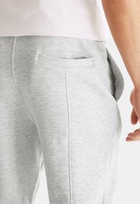 Sivé bavlnené jogger nohavice s jemnou textúrou, vybavené zadnou vreckom a zúženými nohavicami, zobrazené na úrovni pásu s svetlým tričkom nad nimi.