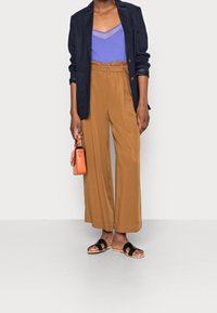 Marinblå blazer, lavendelfärgad linne, bruna vida byxor, svarta sandaler och en liten orange handväska. Vid silhuett med ett flödande material.