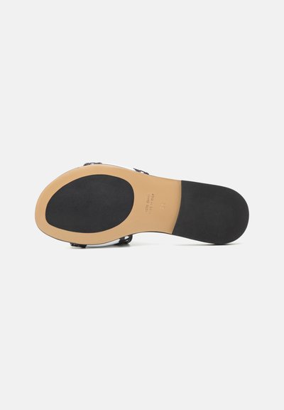 Semelle de chaussure noire avec un bord lisse de couleur marron clair. Présente un logo central et une zone en caoutchouc noir texturé pour l'adhérence. Forme ovale et courbée.