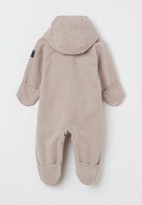 Fleece-Overall in sanftem Beige mit Kapuze, langen Ärmeln und Fußdesign. Mit Bündchenenden und einem kleinen Etikett an der Schulter.