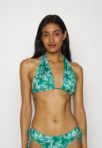 Conjunto de biquíni verde com parte de cima tipo halter e parte de baixo com laço lateral. Apresenta um padrão de folhas tropicais e uma textura lisa e brilhante.